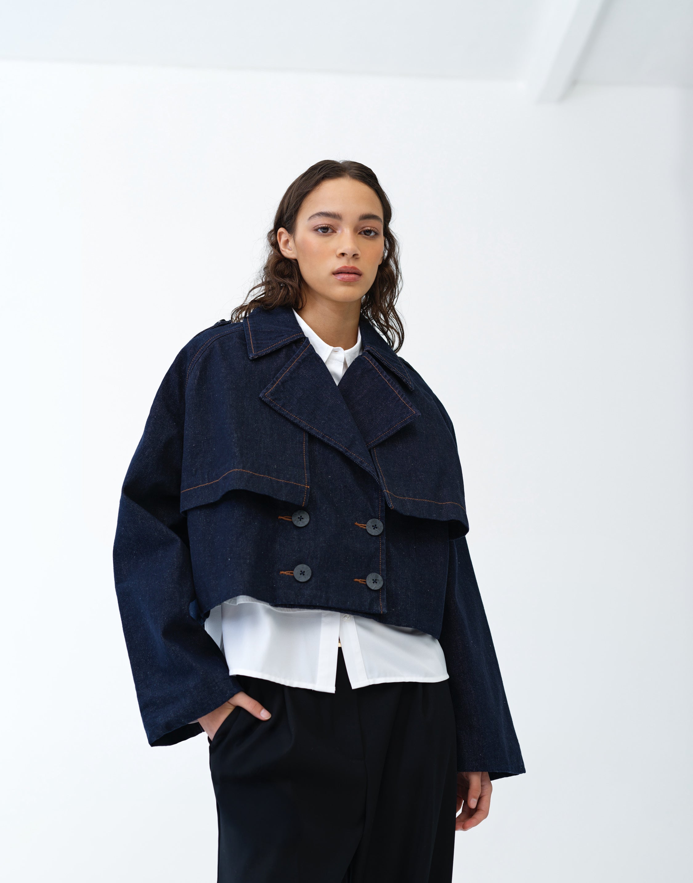 Woman wearing a cropped denim trench coat over a white shirt