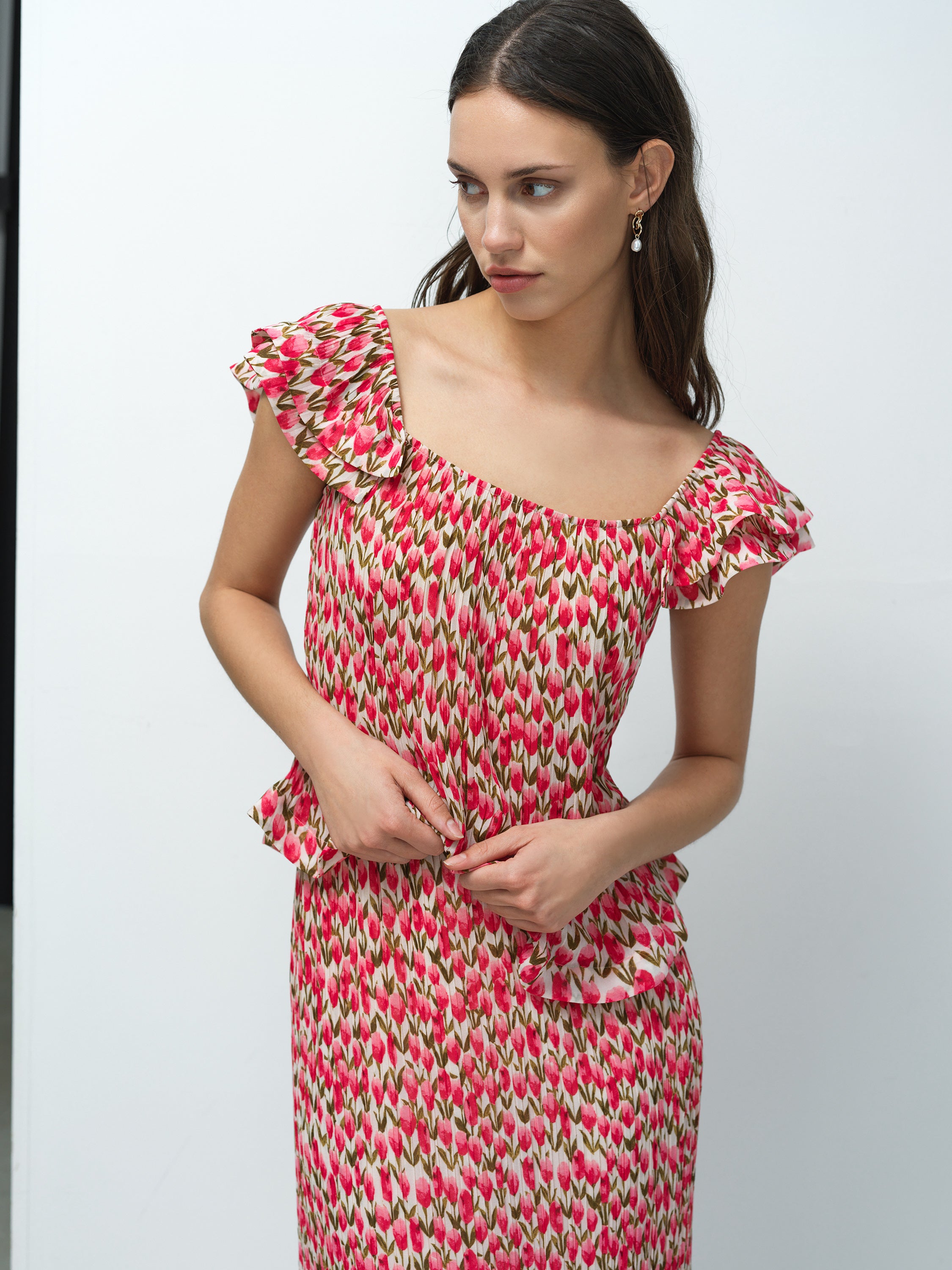 A woman wearing a pink and green floral tulip top with ruffle straps, square neckline and peplum hem.