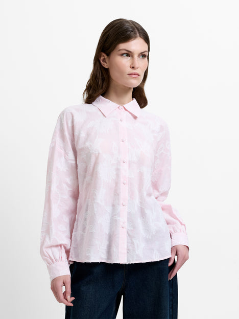 Woman wearing a light pink and white floral jacquard shirt, with dropped long balloon sleeves and a shirt collar