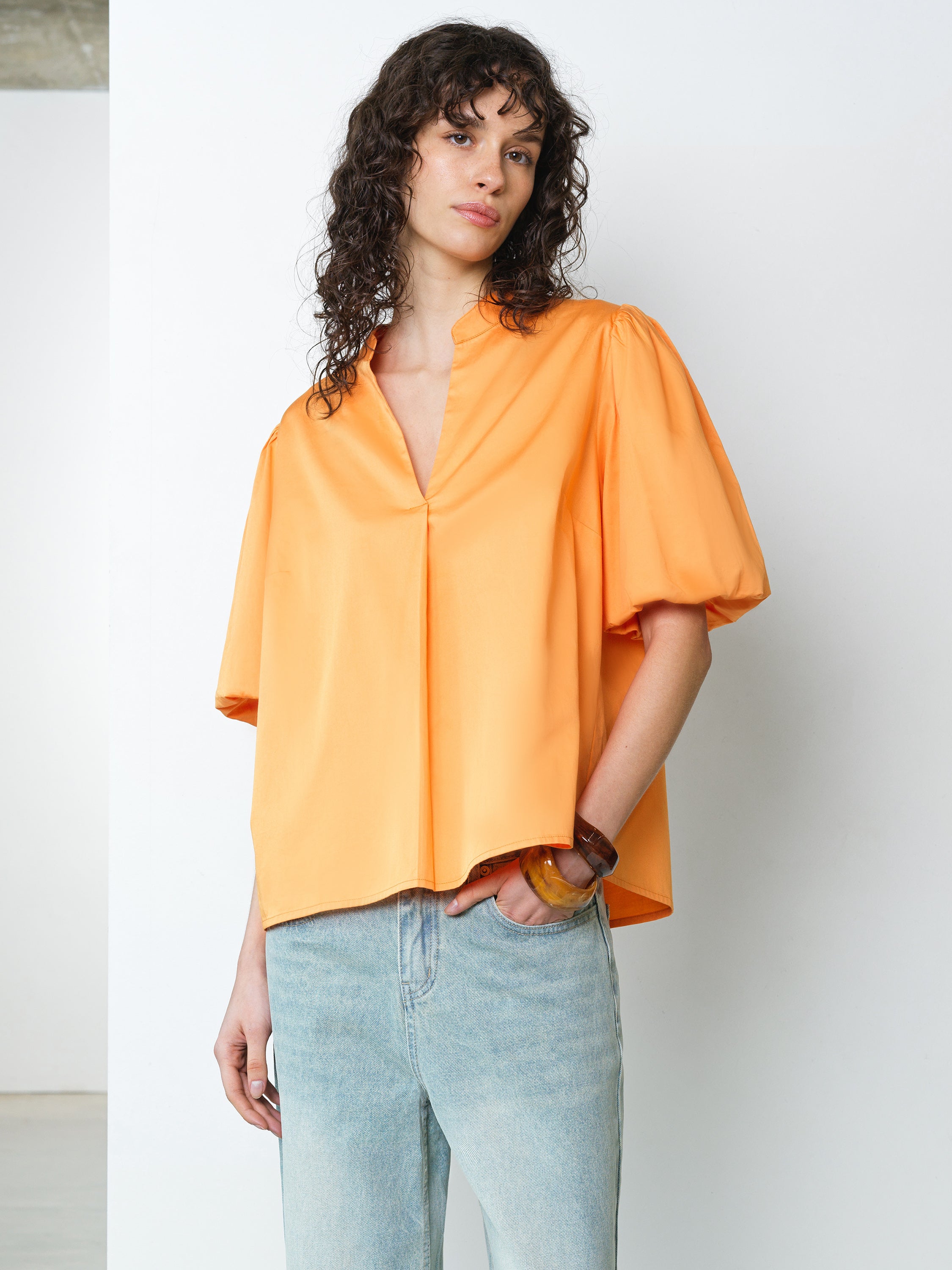 Woman wearing a bright orange popover shirt with short puff sleeves and a V neckline