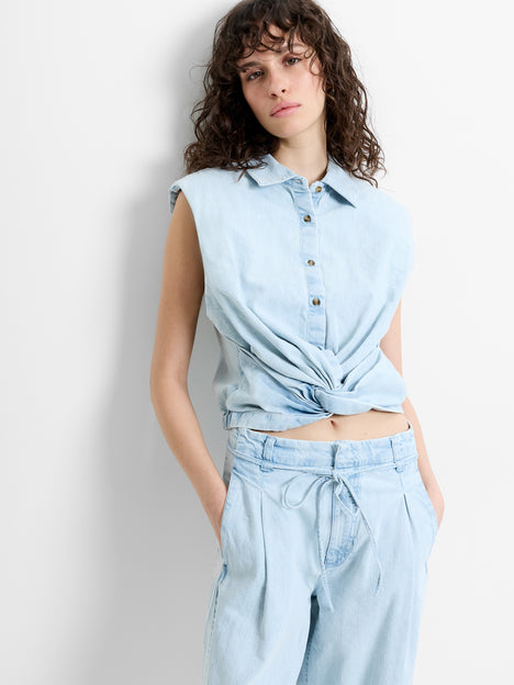 Woman wearing a light blue denim sleeveless top, with padded shoulders and a front twist knot detail