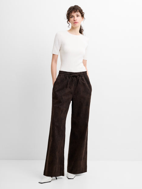 Woman wearing a white top and brown wide-leg snake print trousers with a drawstring waist.