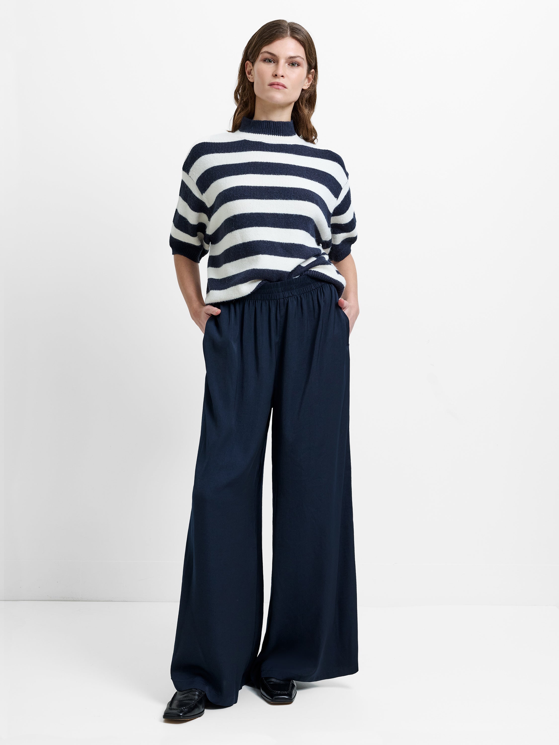 Woman wearing a short sleeve white and navy jumper with wide leg, high waisted elasticated trousers with two side pockets