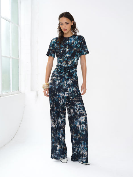 Woman wearing an abstract printed co-ord. A short sleeve draped top and wide leg trousers.