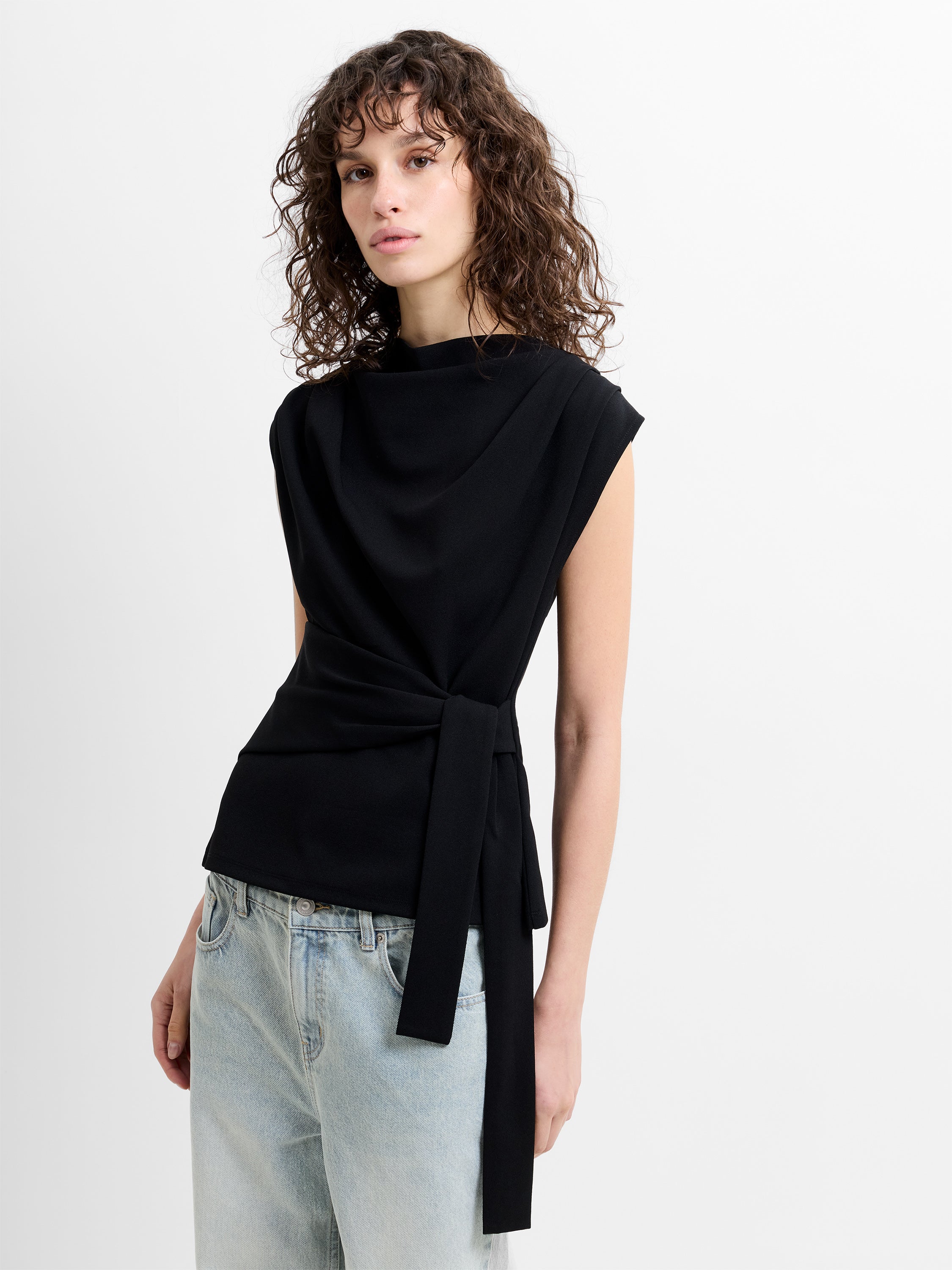 Woman wearing a black sleeveless top with a tie belt and light blue jeans
