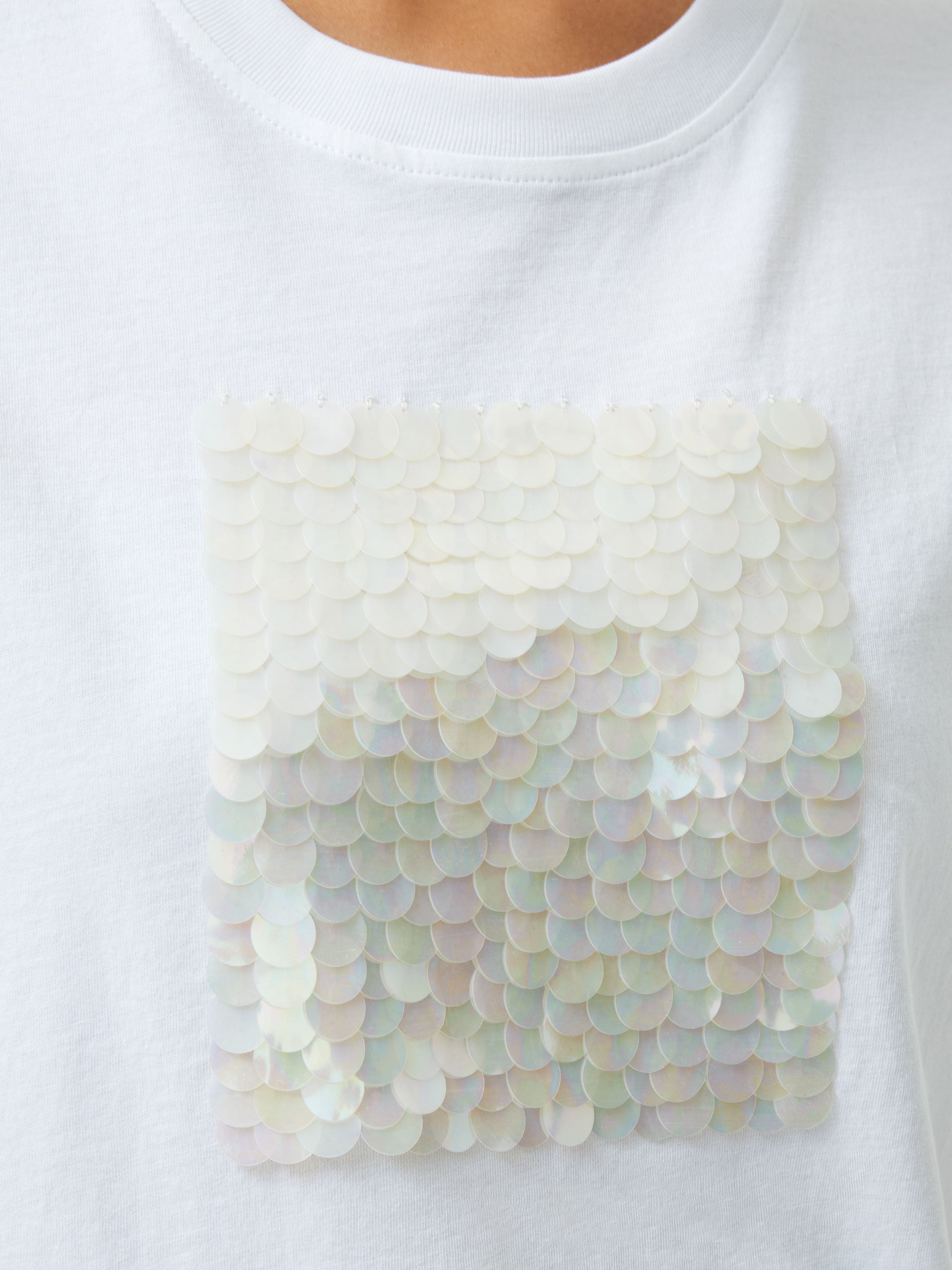 Close-up of the Sequin Jersey Short Sleeve T-Shirt, showcasing iridescent square sequins arranged in neat, overlapping rows on a white base.