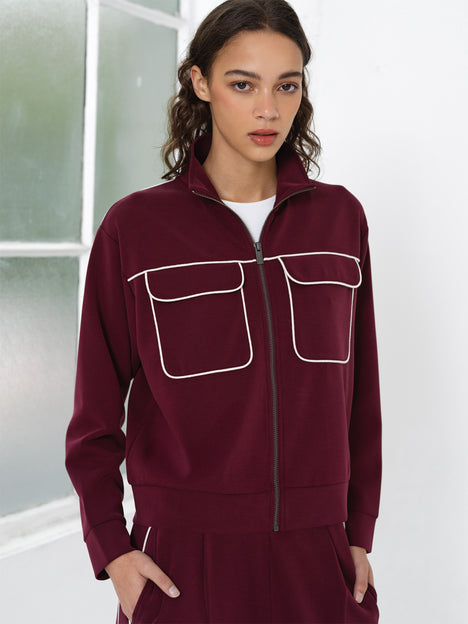 Woman wearing a burgundy jersey zip up sweatshirt with white piping details