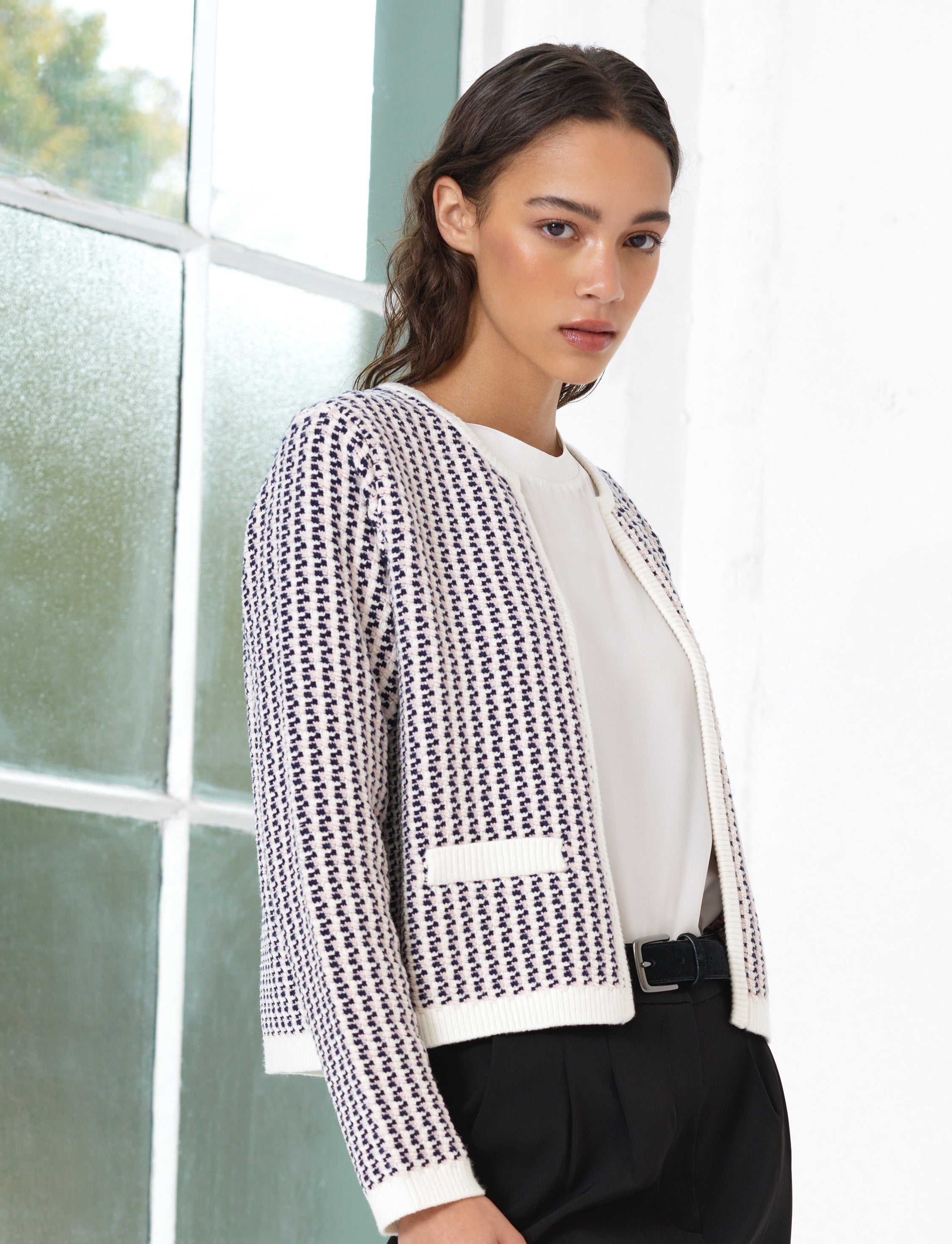 Woman wearing a pink, white and blue abstract patterned cardigan, with long sleeves and a crew neckline